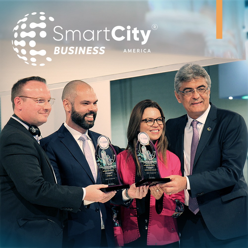 A foto apresenta o logotipo da SmartCity Business America sob a foto de quatro representantes segurando os prêmios pelos resultados do programa Empreenda Fácil e pelo Sistema de Gerenciamento de Zeladoria 